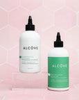 Two bottles of Alcove hair care products on a pink geometric patterned background
