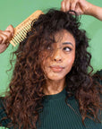 Woman combing her curly hair against a green background