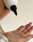 Hand holding a Alcôve Mini Hydrating Shampoo Travel Size dripping liquid onto another hand