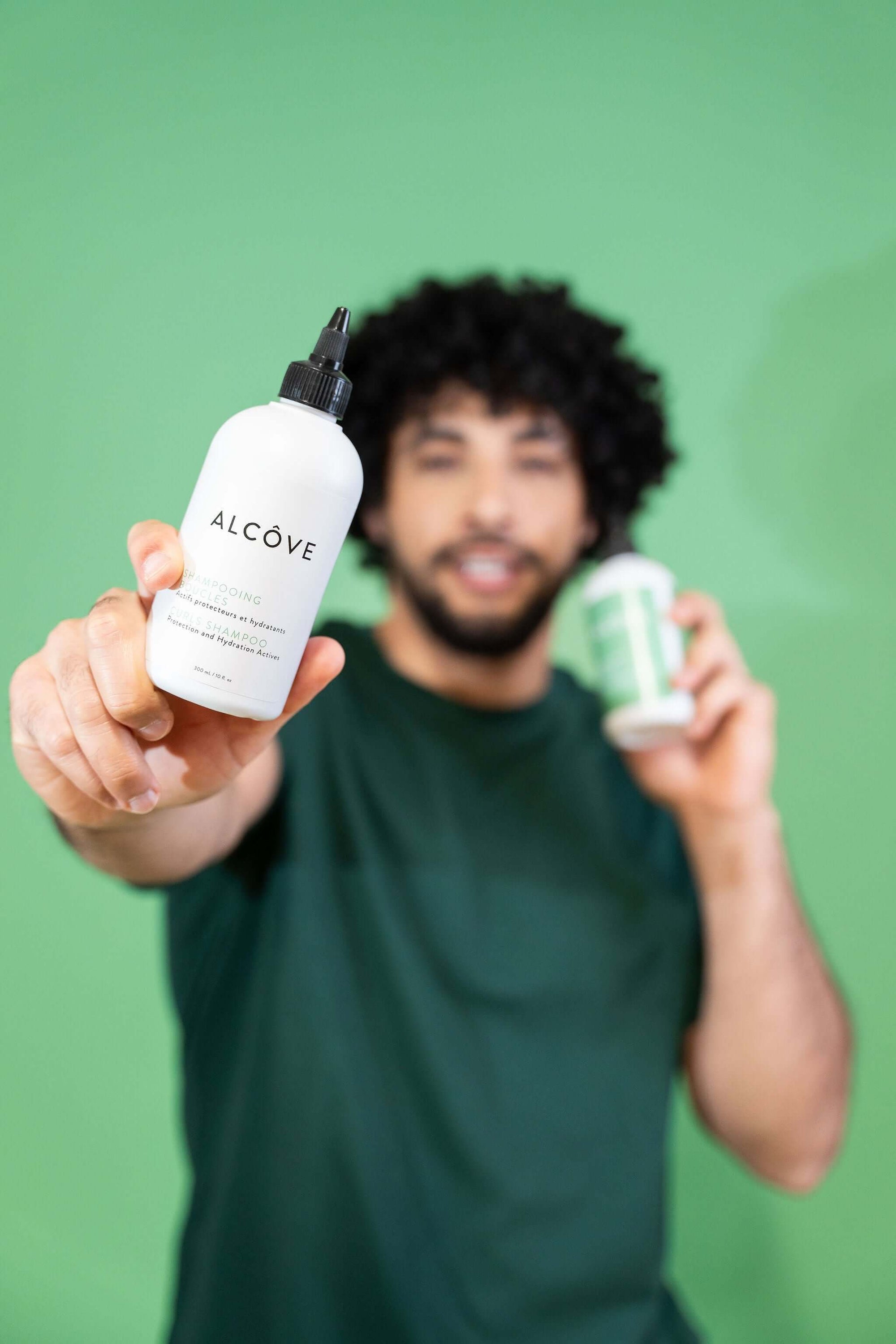 Man holding two bottles of Alcove Hair Curl Shampoo and Conditioner against a green background