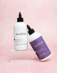 Two bottles of Alcove shampoo and conditioner on a pink geometric patterned background