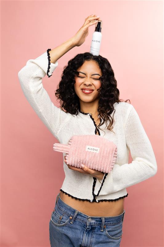 Woman holding an Alcôve white bottle against a pink background