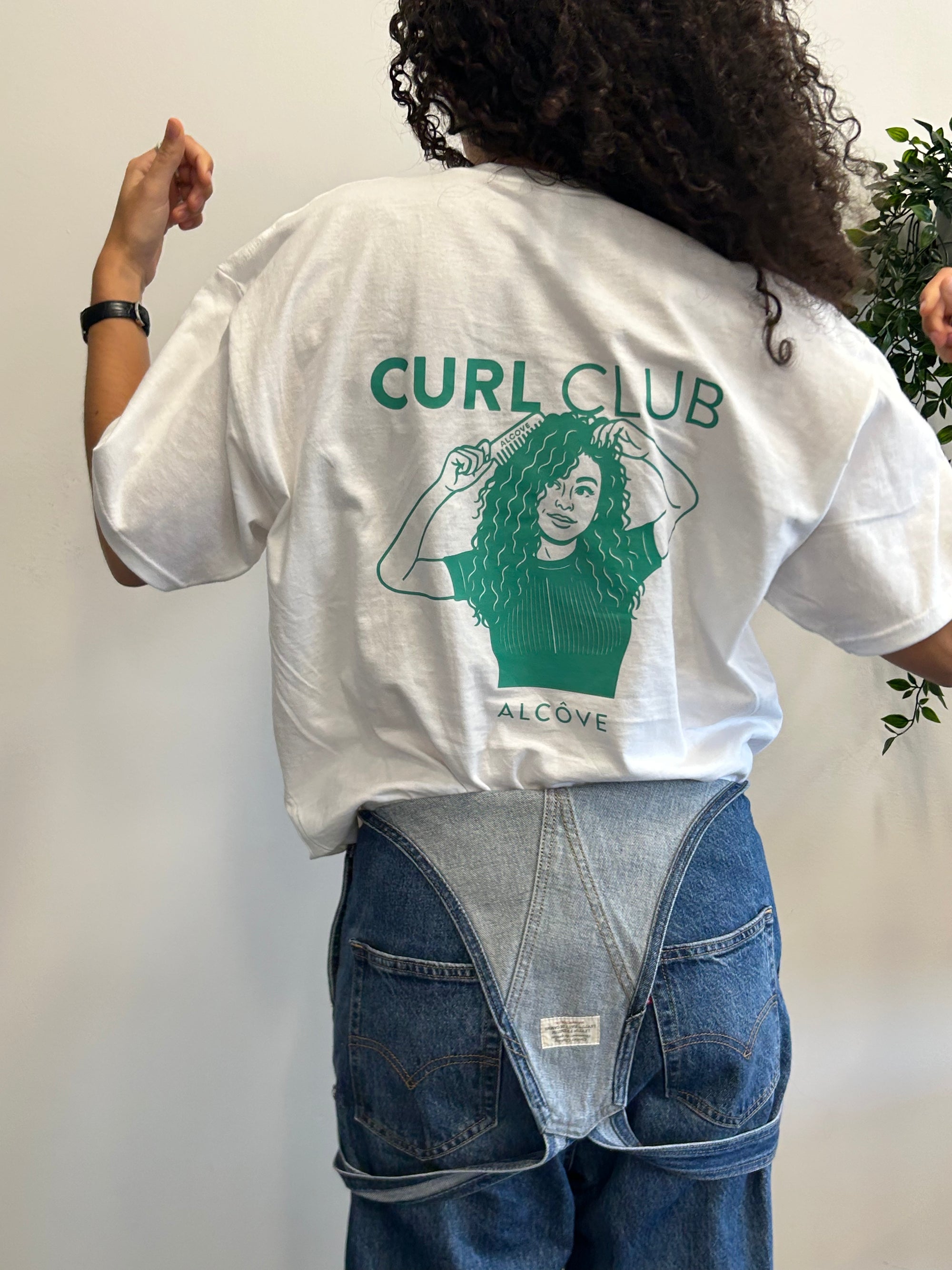 Person wearing a white t-shirt with 'Curl Club' design and text, standing against a plain background.