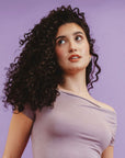 Woman with curly hair wearing a light purple top against a purple background