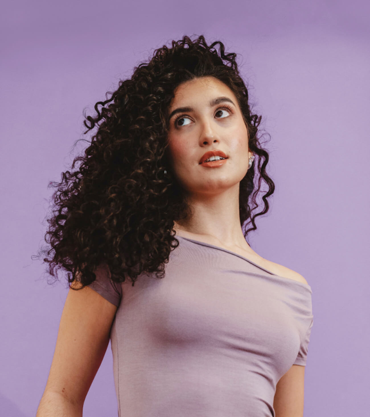 Woman with curly hair wearing a light purple top against a purple background