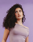 Woman with curly hair wearing a light purple top against a purple background