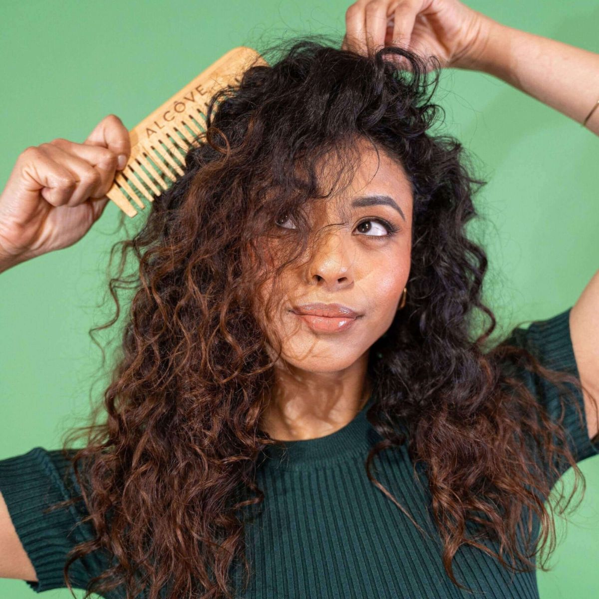 Woman combing her curly hair against a green background