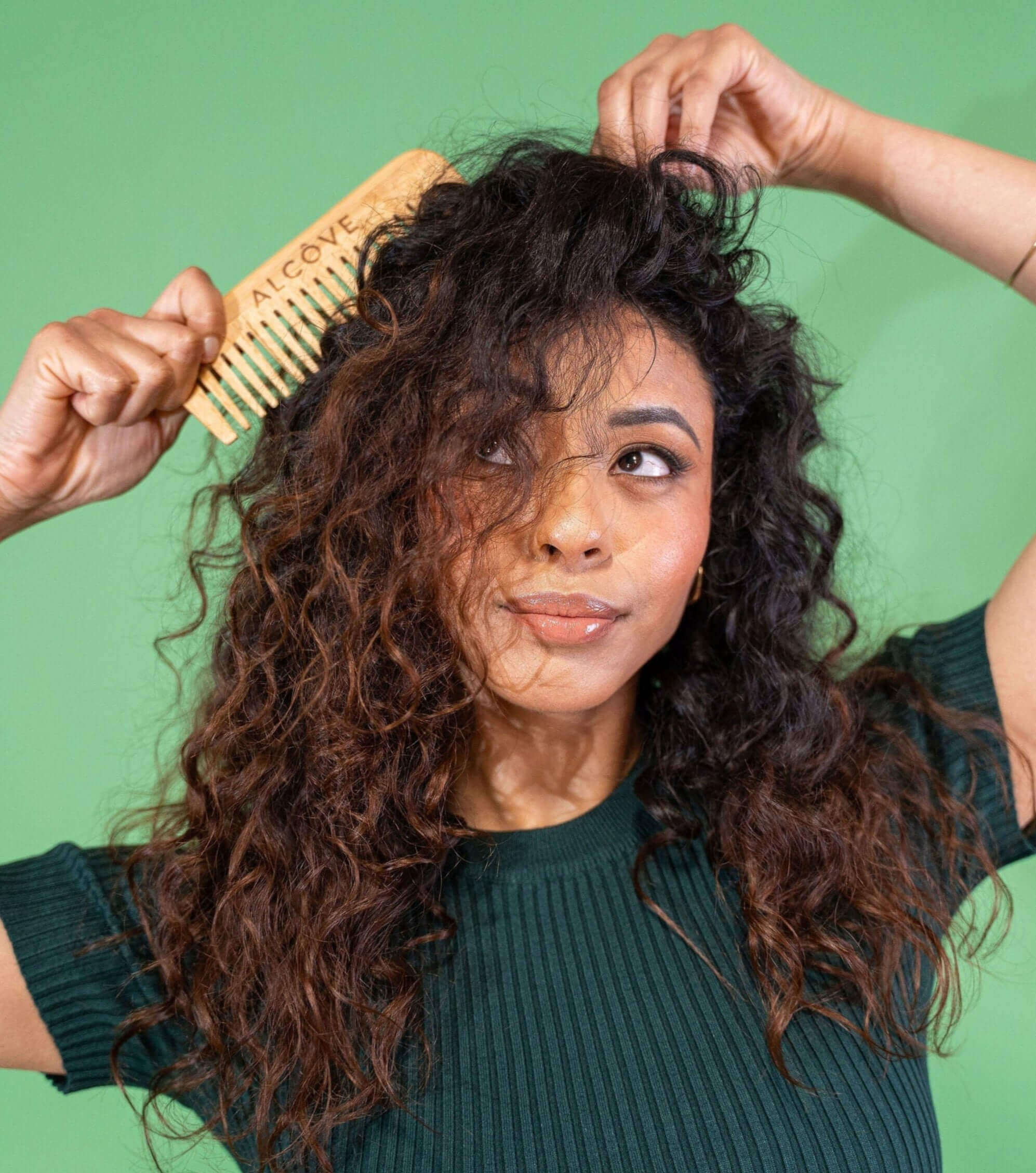 Woman combing her curly hair against a green background