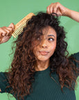 Woman combing her curly hair against a green background