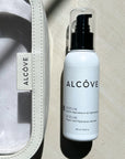 A lifestyle image of the Alcove Hair Serum 100 ml / 3.4 oz next to a Alcxove pouch